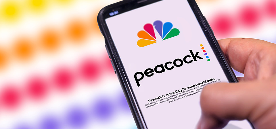 A smartphone with the peacock logo and brand name on display.