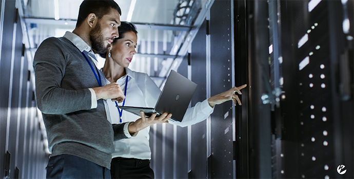 Two people in a server farm holding a laptop.