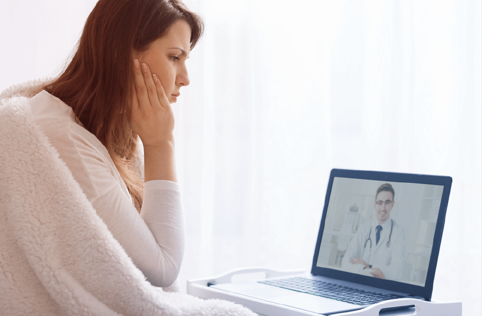 Woman consulting with remote doctor over live stream telehealth appointment on laptop.